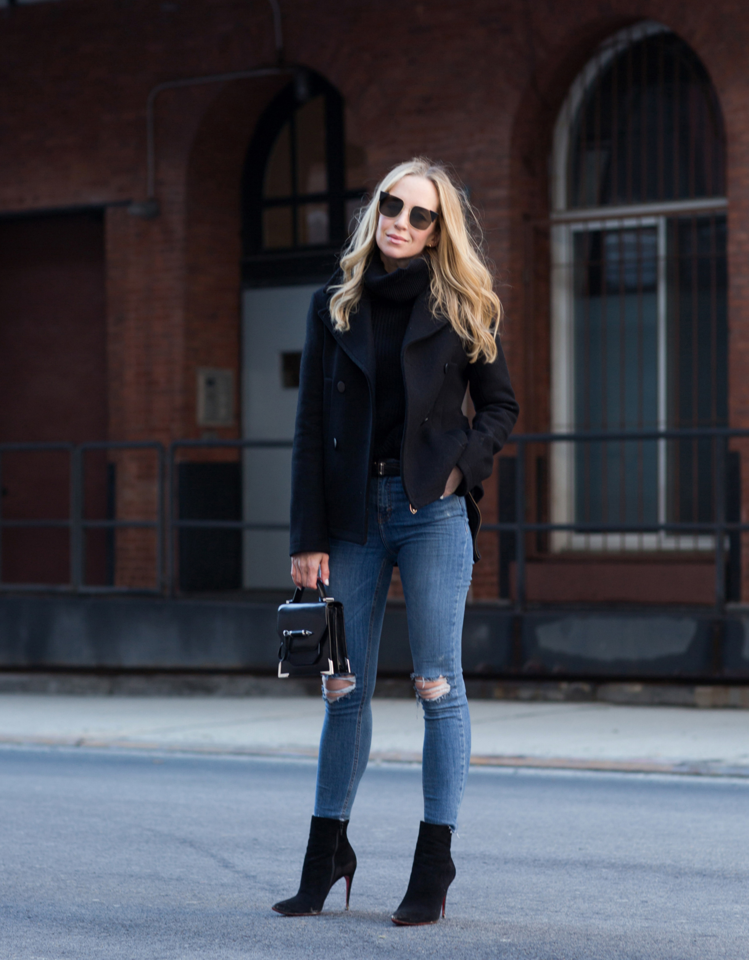 winter work day outfits inspiration - Helena Glazer of Brooklyn Blonde wearing Slate & Stone black Peacoat with black turtleneck sweater, distressed denim, Louboutin boots, Fendi Sunglasses, and Mackage handbag