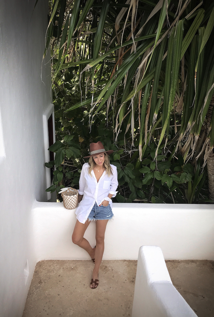 woman wearing denim shorts, white top, and hat