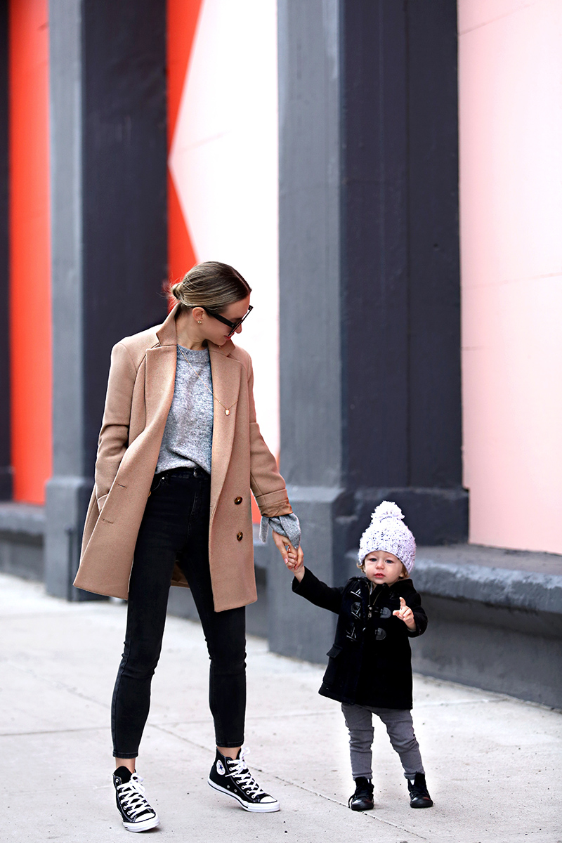 woman wearing black pants, grey shirt, and coat with her child