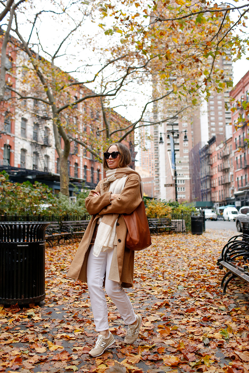 woman in brown coat, white jeans, and sneakers