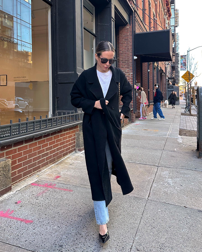woman walking and wearing Prada Moddellerie Mary Jane Pumps, white shirt, and black coat