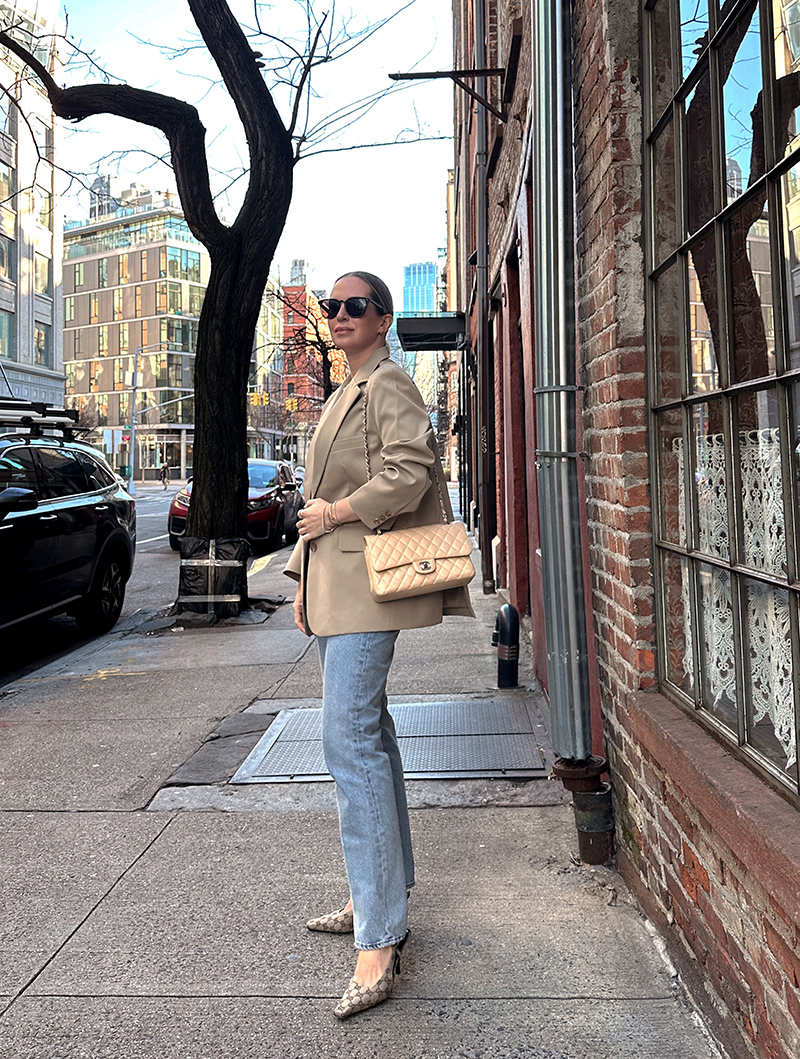 woman standing outside a cafe and wearing Gucci Aria Slingbacks, jeans, and oversized jacket