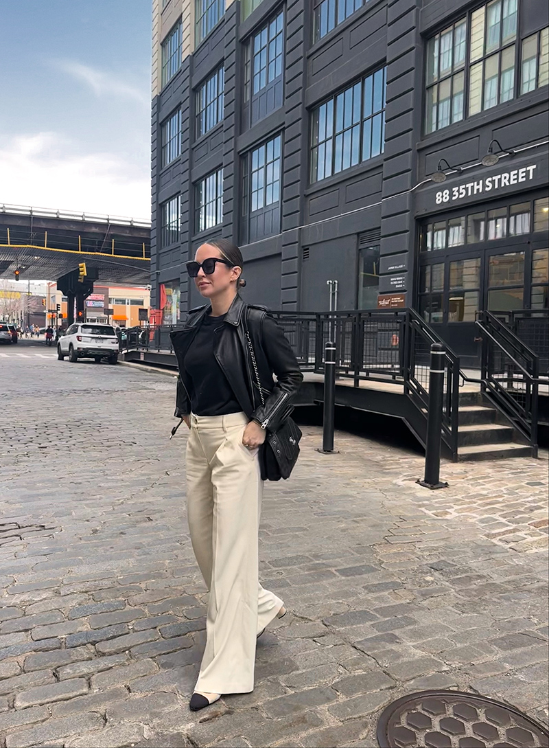 woman in black top and leather jacket and beige trousers